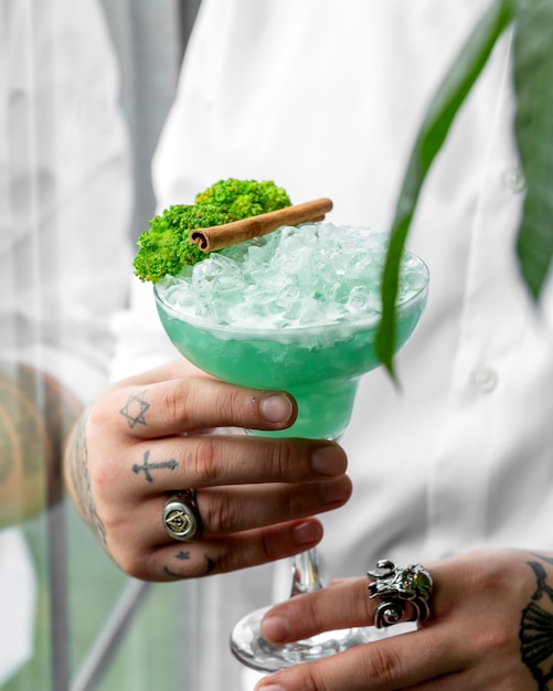 Cameriere che tiene un bicchiere di cocktail verde guarnito con broccoli e stecca di cannella