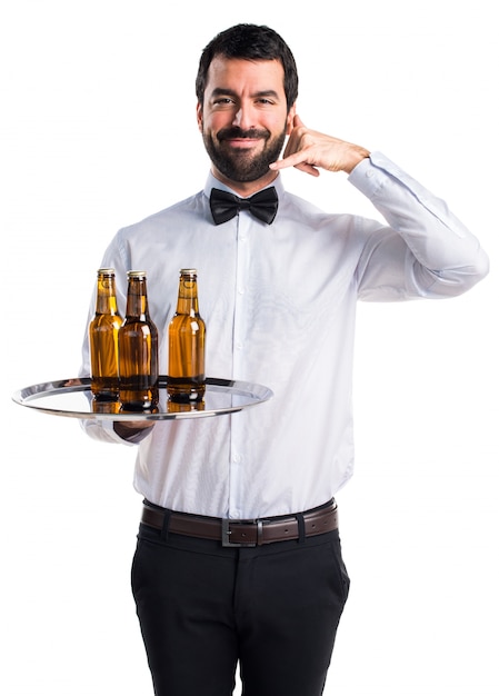 Cameriere con bottiglie di birra sul vassoio facendo il gesto del telefono