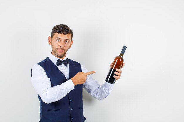 Cameriere in camicia, giubbotto puntare il dito alla bottiglia di alcol, vista frontale.