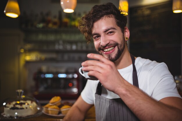 cameriere sorridente con una tazza di caffè al banco in caffetteria ©