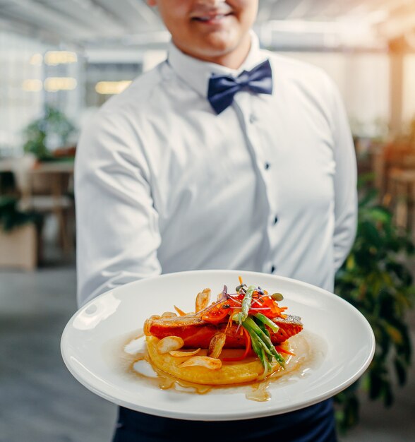 camerieri con piatto di salmone grigliato, purè di patate, condito con caviale rosso, asparagi