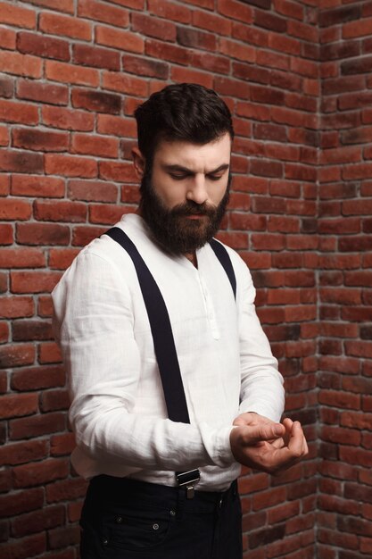 Camicia di correzione del giovane uomo bello sul muro di mattoni.