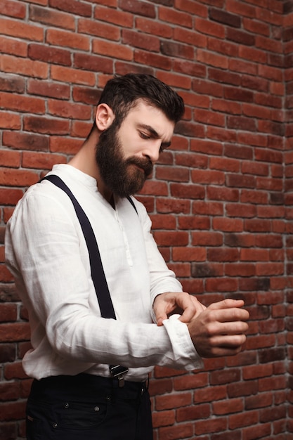 Camicia di correzione del giovane uomo bello sul muro di mattoni.