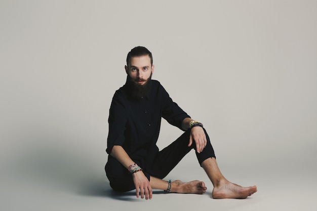 Camicia nera dell'uomo barbuto di stile dei pantaloni a vita bassa in studio sopra fondo bianco