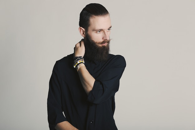 Camicia nera dell'uomo barbuto di stile dei pantaloni a vita bassa in studio sopra fondo bianco