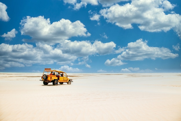 Camion giallo che guida sul terreno sabbioso sotto il cielo blu nuvoloso