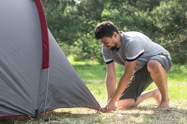 Campeggio, viaggio, turismo, concetto di escursione - giovane che installa tenda nella foresta.