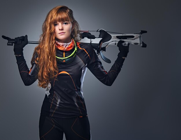 Campione di biathlon femminile rossa che mira con una pistola competitiva in uno studio su sfondo grigio. Campione di biathlon femminile rossa che punta con una pistola competitiva in uno studio su sfondo grigio.