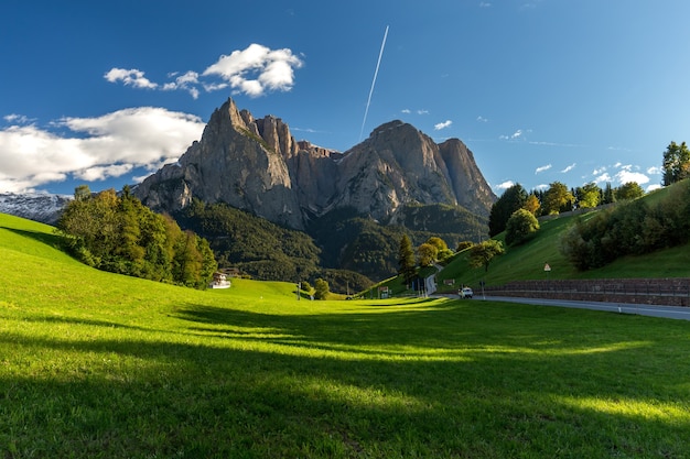Campo circondato da rocce ricoperte di verde sotto un cielo azzurro e luce solare in Italia