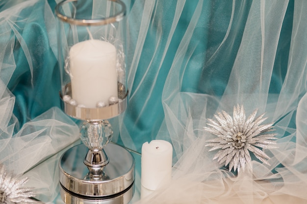 Candela bianca nel candeliere di vetro con seta acquamarina decorativa