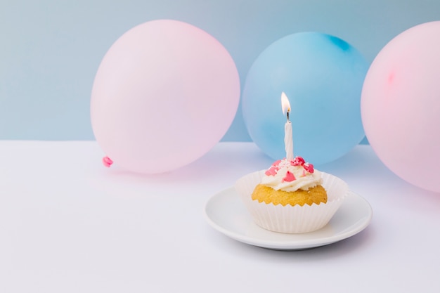 Candela sul cupcake sul piatto con palloncini rosa e blu