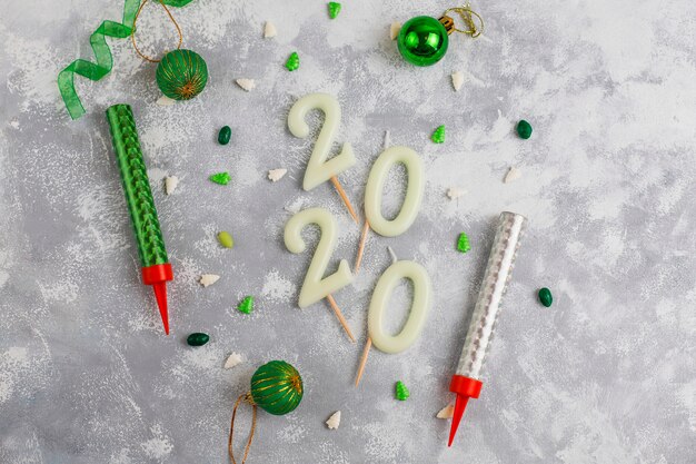Candele a forma di numeri 2020 come simbolo del nuovo anno accanto a caramelle scintillanti a forma di Natale su un tavolo grigio. Vista dall'alto, piatto