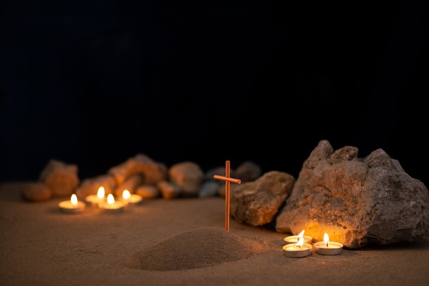 Candele accese con pietre e piccola tomba sulla sabbia come funerale di morte di memoria