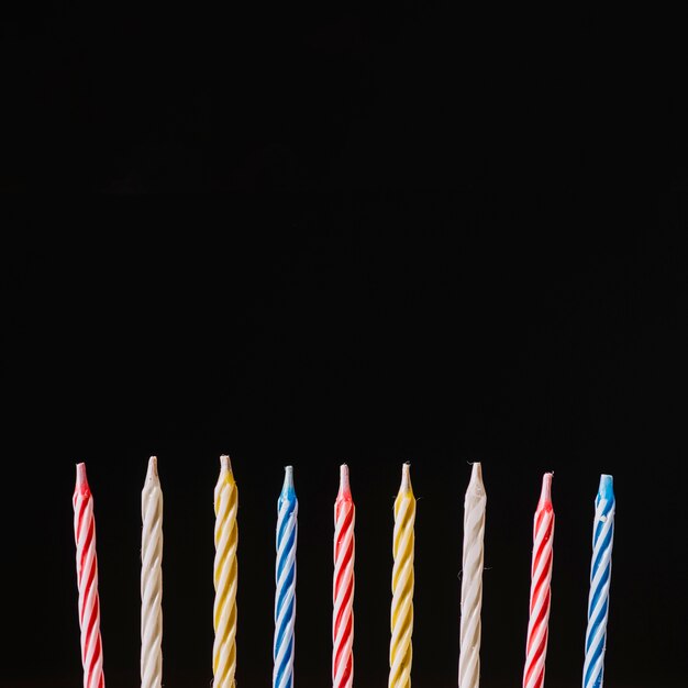 Candele variopinte a strisce di compleanno contro fondo nero