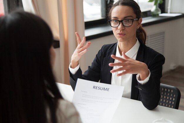 Candidato femmina millenario fiducioso in bicchieri che parlano al colloquio di lavoro