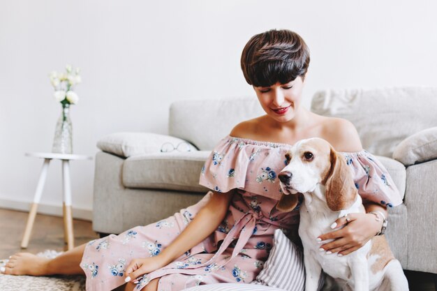 Cane beagle bianco con orecchie marroni che guarda lontano mentre sorridente ragazza bruna seduta accanto