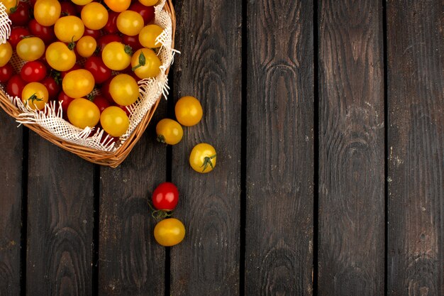 Canestro interno maturo fresco giallo e rosso dei pomodori sul pavimento rustico di legno
