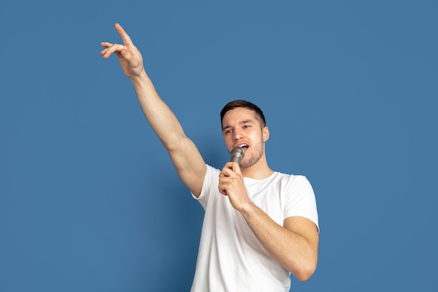 Cantando come celebrità, star. Ritratto di giovane uomo caucasico su sfondo blu.