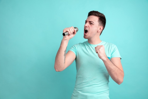 Cantare come una star. Il ritratto del giovane caucasico isolato sulla parete blu. Bellissimo modello maschile in stile casual, colori pastello. Concetto di emozioni umane, espressione facciale