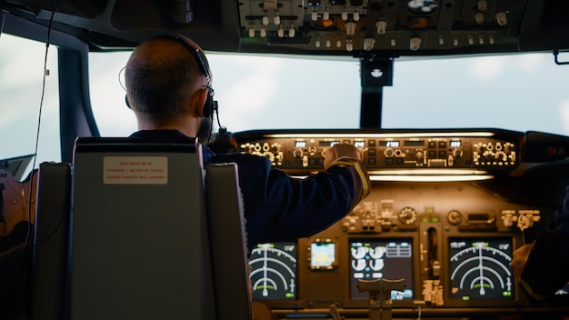 Capitano di linea maschile che fissa i pulsanti di altitudine e longitudine, utilizzando il comando di navigazione del cruscotto e il pannello di controllo. Aereo volante con equipaggio e bussola radar, motore elettrico e parabrezza.