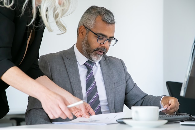 Capo concentrato che analizza i rapporti dei manager, leggendo e rivedendo i documenti mentre è seduto al posto di lavoro. Concetto di comunicazione aziendale