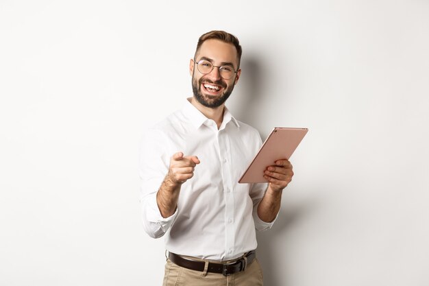 Capo felice e soddisfatto che elogia il buon lavoro, legge sulla tavoletta digitale e indica la fotocamera, in piedi