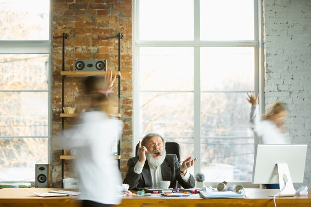 Capo stanco che riposa al suo posto di lavoro mentre le persone occupate si spostano vicino a sfocato. Impiegato, manager che lavora, beve caffè e dà indicazioni ai suoi colleghi. Affari, lavoro, concetto di carico di lavoro.