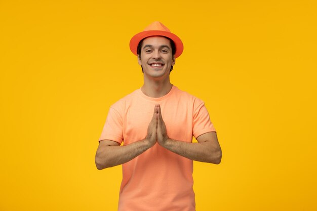 Cappello arancione carino giovane ragazzo in camicia arancione con il cappello che prega e sorridente