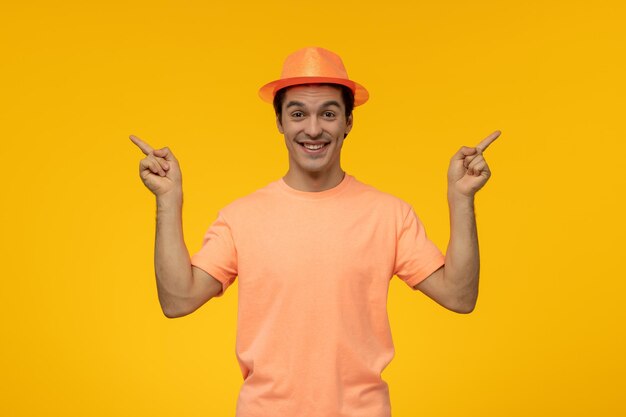 Cappello arancione felice bel ragazzo carino in maglietta arancione con il cappello che punta le dita verso l'alto
