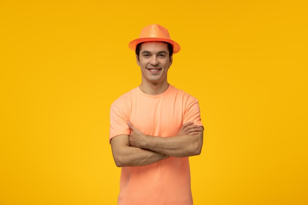 Cappello arancione giovane ragazzo carino sorridente con le mani incrociate in maglietta arancione