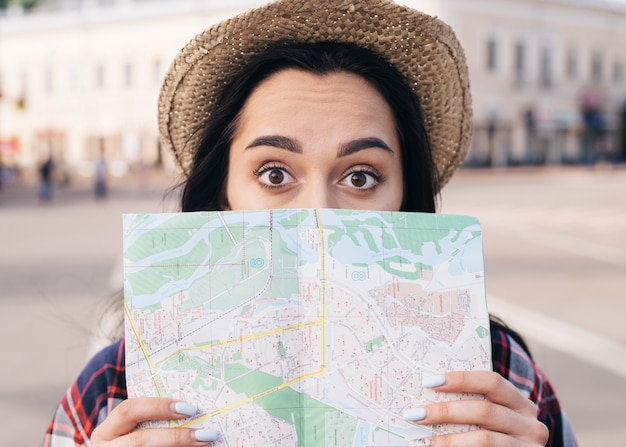 Cappello da portare sorpreso della giovane donna che copre la sua bocca di mappa all'aperto