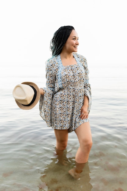 Cappello della tenuta della donna della foto a figura intera in mare