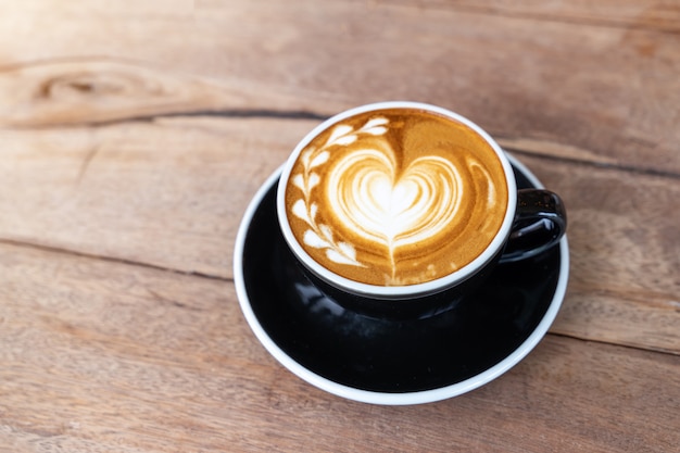 Cappuccino caldo del caffè di arte in una tazza sul fondo di legno della tavola con lo spazio della copia