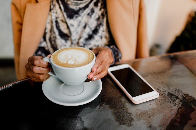 Cappuccino della tazza di caffè in mani della donna.