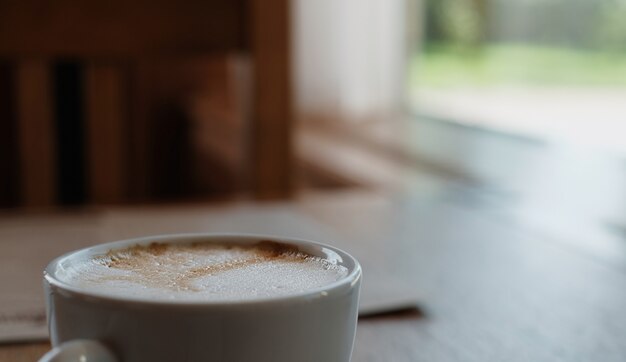 Cappuccino o caffè latte su un tavolo di legno. Primo piano, messa a fuoco selettiva, luce solare dalla finestra. Idea pausa caffè, pausa caffè