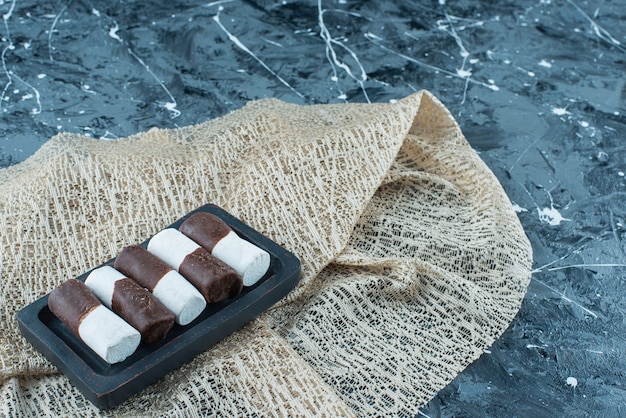 Caramelle a due colori su un piatto di legno su una tovaglia, sul tavolo blu.