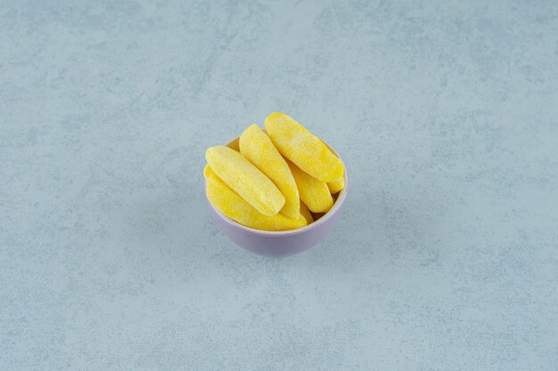 Caramelle da masticare a forma di banana in ciotola su superficie bianca