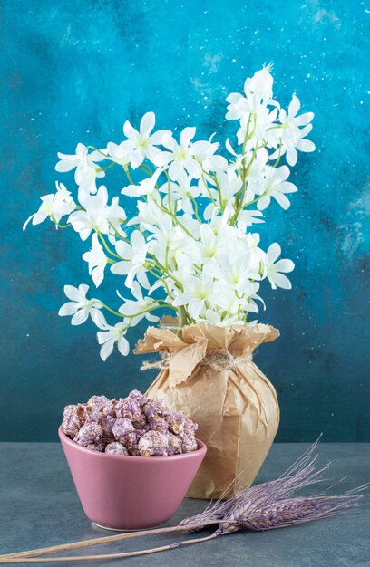 Caramelle di popcorn in una ciotola, gambi di grano viola e gigli bianchi in un vaso su sfondo blu. Foto di alta qualità
