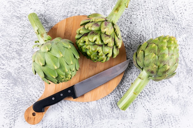 Carciofi su un tagliere con coltello vista dall'alto su un grigio chiaro