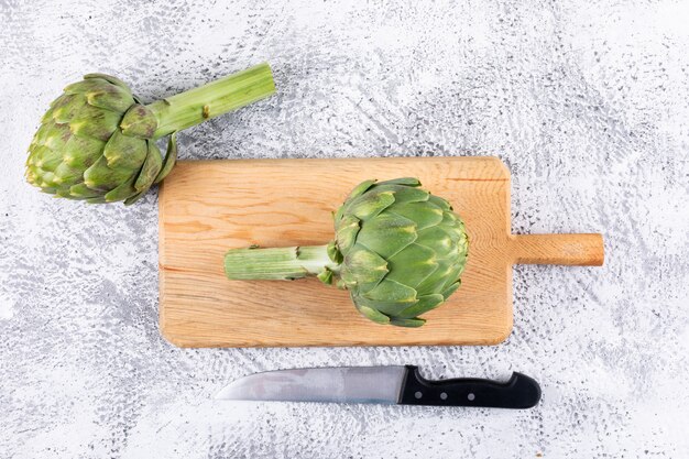 Carciofi vista dall'alto sul tagliere con coltello su sfondo grigio chiaro. orizzontale