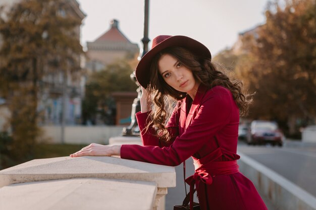 Carina bella donna alla moda in vestito viola che cammina nella via della città, tendenza di moda primavera estate autunno stagione indossando il cappello, tenendo la borsa