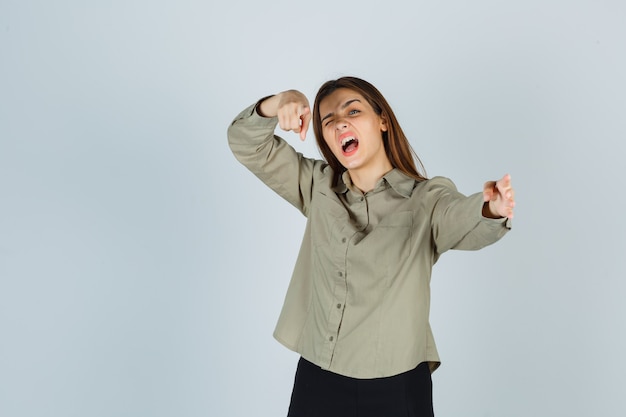 Carina giovane donna in camicia, gonna che punta alla telecamera mentre urla, sbatte le palpebre e sembra energica, vista frontale.