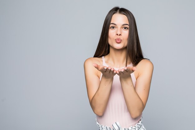 Carino accattivante donna soffia bacio, dimostra amore al fidanzato o dice addio a distanza, isolato sopra il muro bianco La giovane donna attraente mostra simpatia a qualcuno