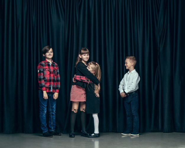 Carino bambini alla moda in studio scuro. Le belle ragazze adolescenti e il ragazzo in piedi insieme