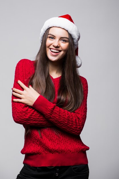 Carino giovane donna caucasica che indossa il cappello della Santa e guanti in posa sorridente contro il muro grigio chiaro. Concetto di Natale e Capodanno. Copia spazio disponibile.