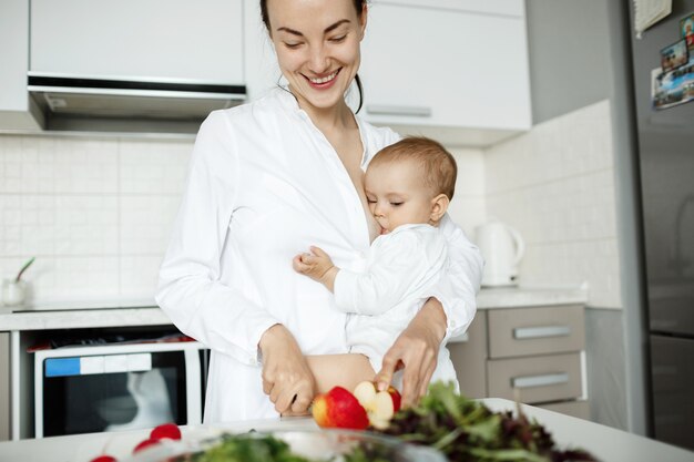 Carino giovane madre allattare il bambino durante la cottura di una sana colazione