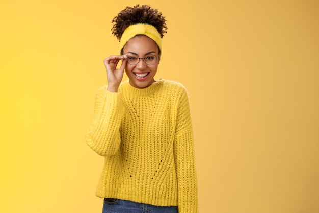 Carino intelligente migliore studentessa universitaria afro-americano tocco occhiali naso sorridente ampiamente lavoro part-time tutor bambini lezioni di inglese sorridente amichevole in piedi sfondo giallo maglione, fascia.