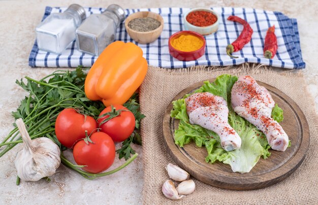 Carne cruda di cosce di pollo con verdure su una tavola di legno