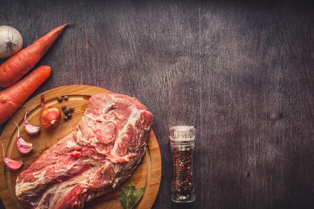 Carne di maiale cruda su un tagliere su una superficie di legno scura e spezie per cucinare. Sfondo alimentare con spazio di copia. Tonico