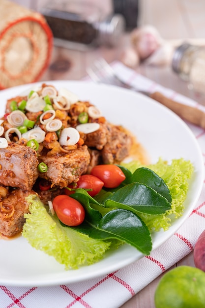 Carne di maiale piccante tritata con i pomodori e la lattuga su un piatto bianco su una tavola di legno.